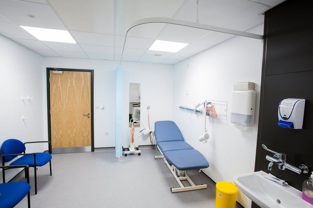 Medical examination room with blue examination table, sink, and chairs.