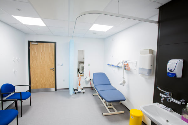 Medical examination room with blue examination table, sink, and chairs.