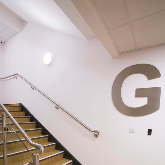 Staircase with metal handrails against a white wall with a large 'G' logo.