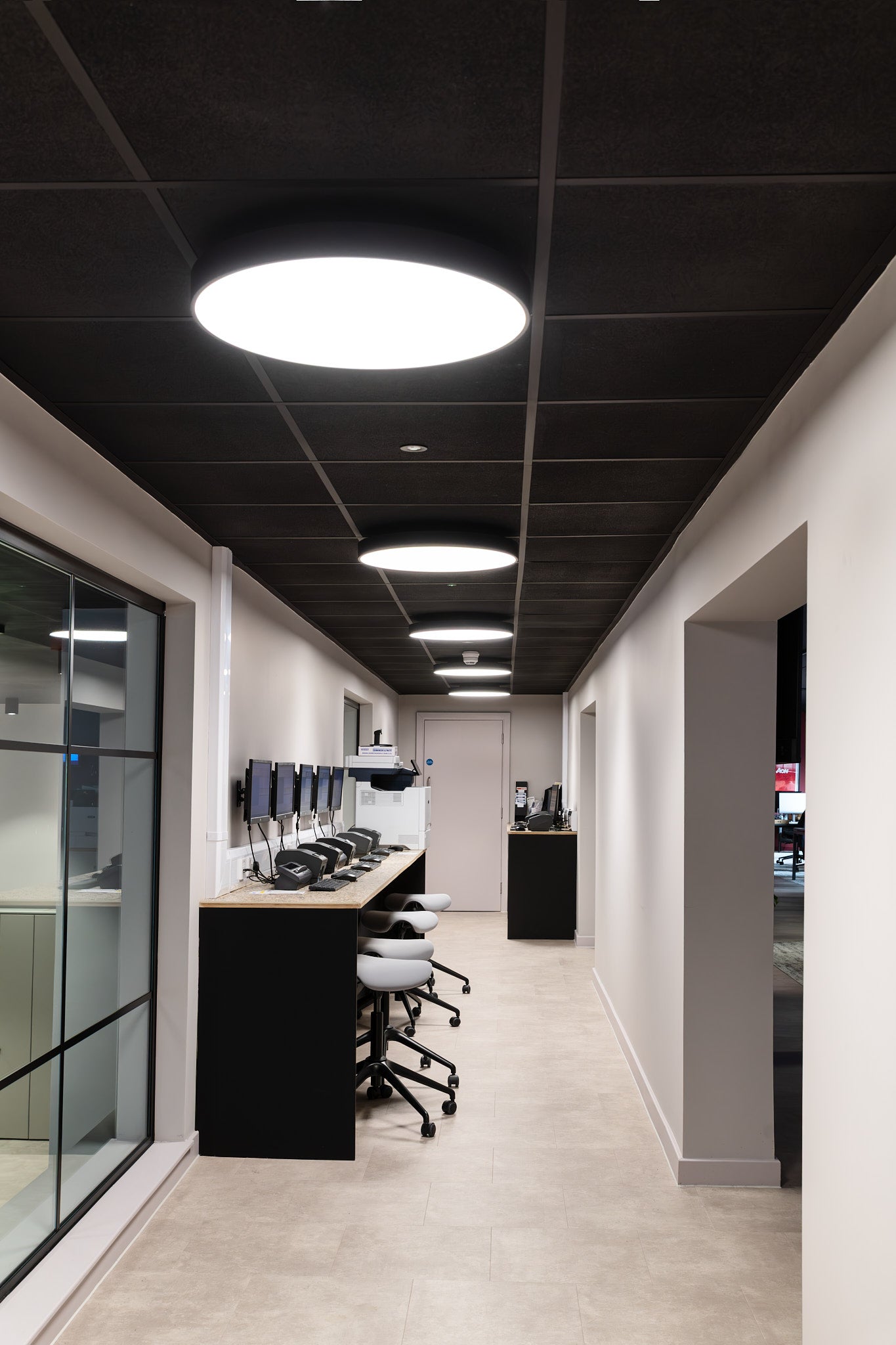 Modern office hallway with black ceiling panels and white walls.