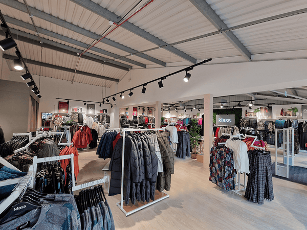 Interior of a clothing store with racks of clothes and a 'Klass' sign.