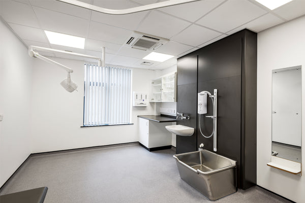 Modern medical examination room with sink, cabinets, and medical equipment.